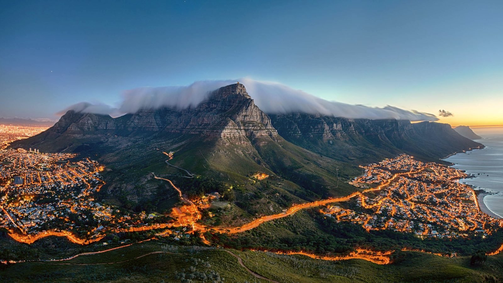 Cape Town and Table Mountain at dusk, with the lit city below the mountain.